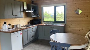 A compact kitchen with grey cabinets, a microwave, a coffee maker, and a sink. There's a window with a view of greenery outside.