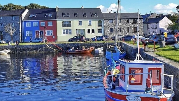 A harbor with boats docked, a stone wall, and colorful buildings.