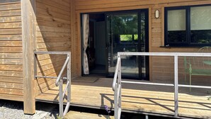 A wooden cabin with a glass door entrance, a small outdoor seating area, and a wooden deck.