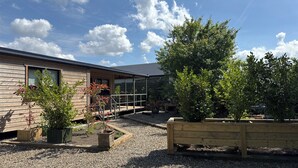A wooden house with a covered porch, gravel driveway, and various potted plants.
