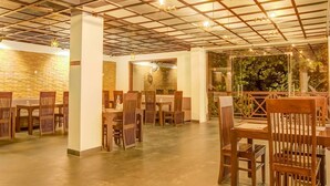 A spacious restaurant with a high ceiling featuring a grid pattern and hanging lights. Tables and chairs are arranged for dining. - Aavaas Hill Resort (Lansdowne)