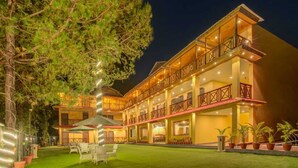 A multi-story hotel with a balcony on the second floor, outdoor seating, and a well-lit entrance. - Aavaas Hill Resort (Lansdowne)