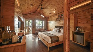 A wooden cabin bedroom with a bed, a small table with bottles, a coffee maker, and a safe. - Aavaas Hill Resort (Lansdowne)