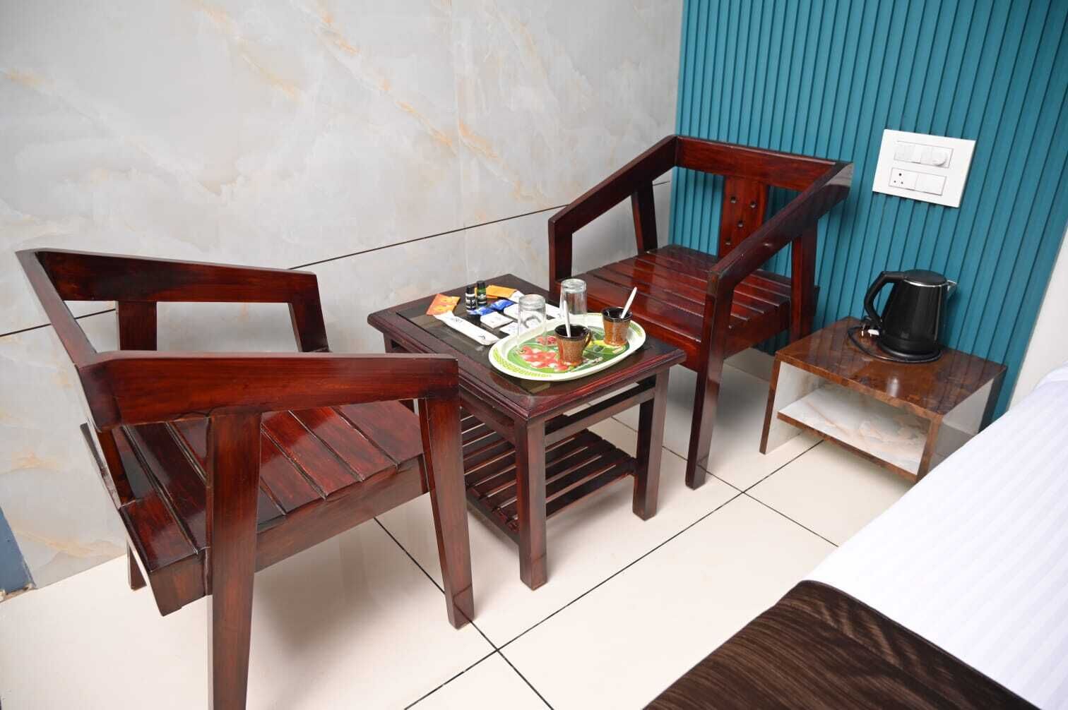 Een kleine kamer met twee houten stoelen, een tafeltje met eten erop, een waterkoker en een stopcontact aan de muur.