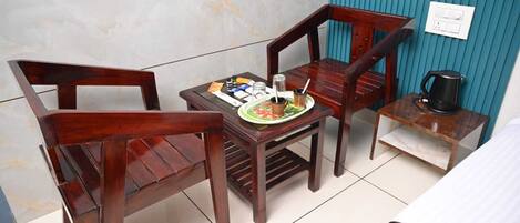 Een kleine kamer met twee houten stoelen, een tafeltje met eten erop, een waterkoker en een stopcontact aan de muur.
