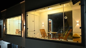 Une chambre d’hôtel moderne dotée de grandes fenêtres, d’une chaise en bois, d’une petite table et d’un élément architectural original.