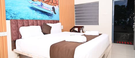 Habitación de hotel con una cama grande, un cuadro de una playa, una ventana con vistas y una puerta que da a un balcón.