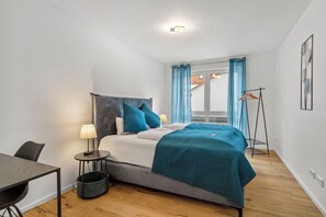 Un dormitorio con cama, mesita de noche, lámpara y una silla pequeña.