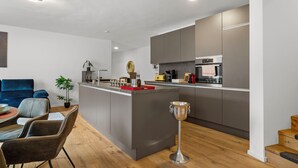 A modern kitchen with a central island, built-in appliances, and a dining area with a blue sofa and chairs. - Lit Living-Luxury-Box Spring - Parking (Hemsbach)
