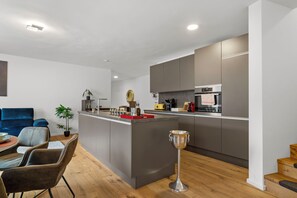 Une cuisine moderne dotée d’un îlot central, d’appareils électroménagers intégrés et d’un coin repas avec un canapé et des chaises bleus.