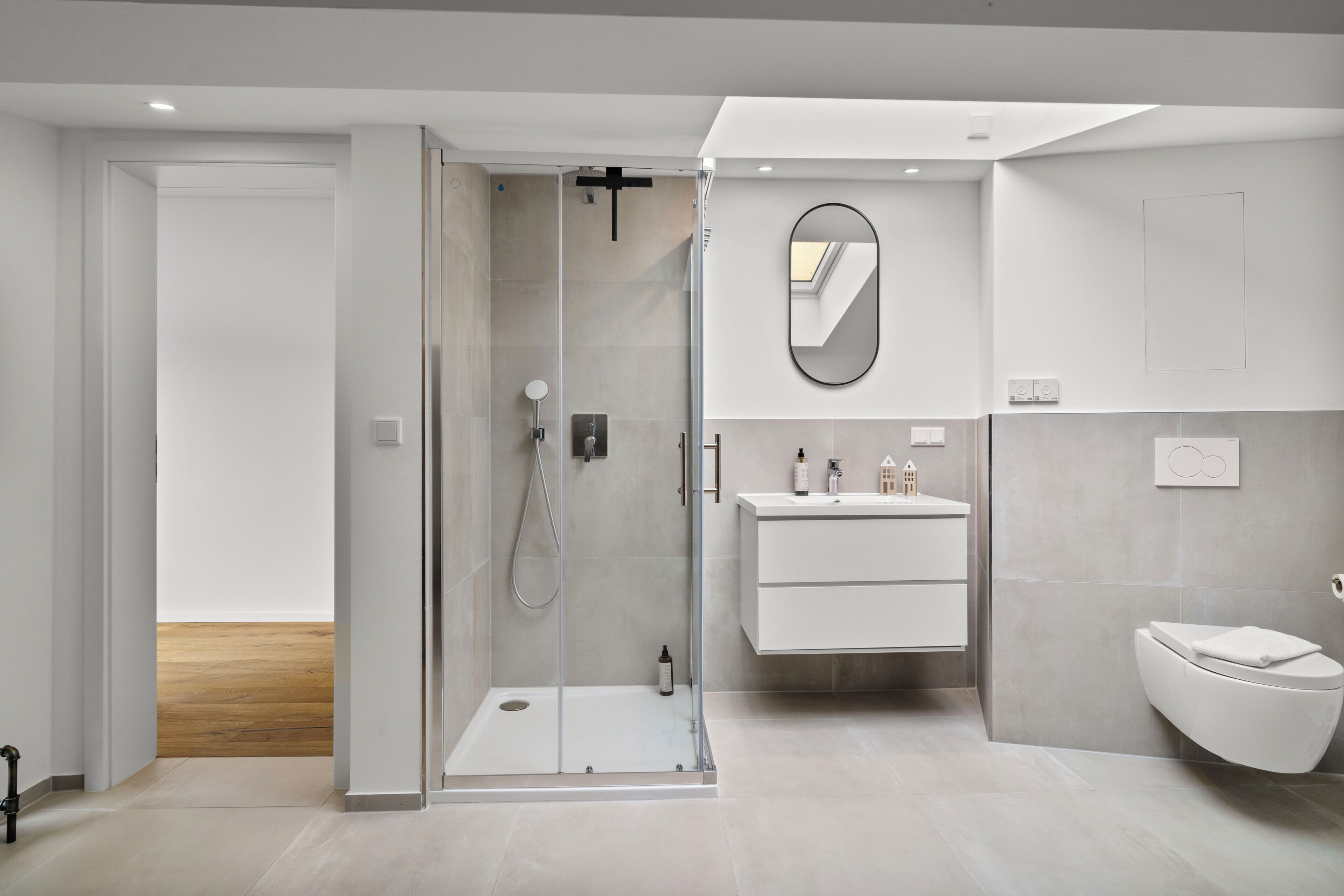 Ein modernes Badezimmer mit einer Duschkabine aus Glas, einem weißen Waschtisch mit Spiegel und einer weißen Toilette.