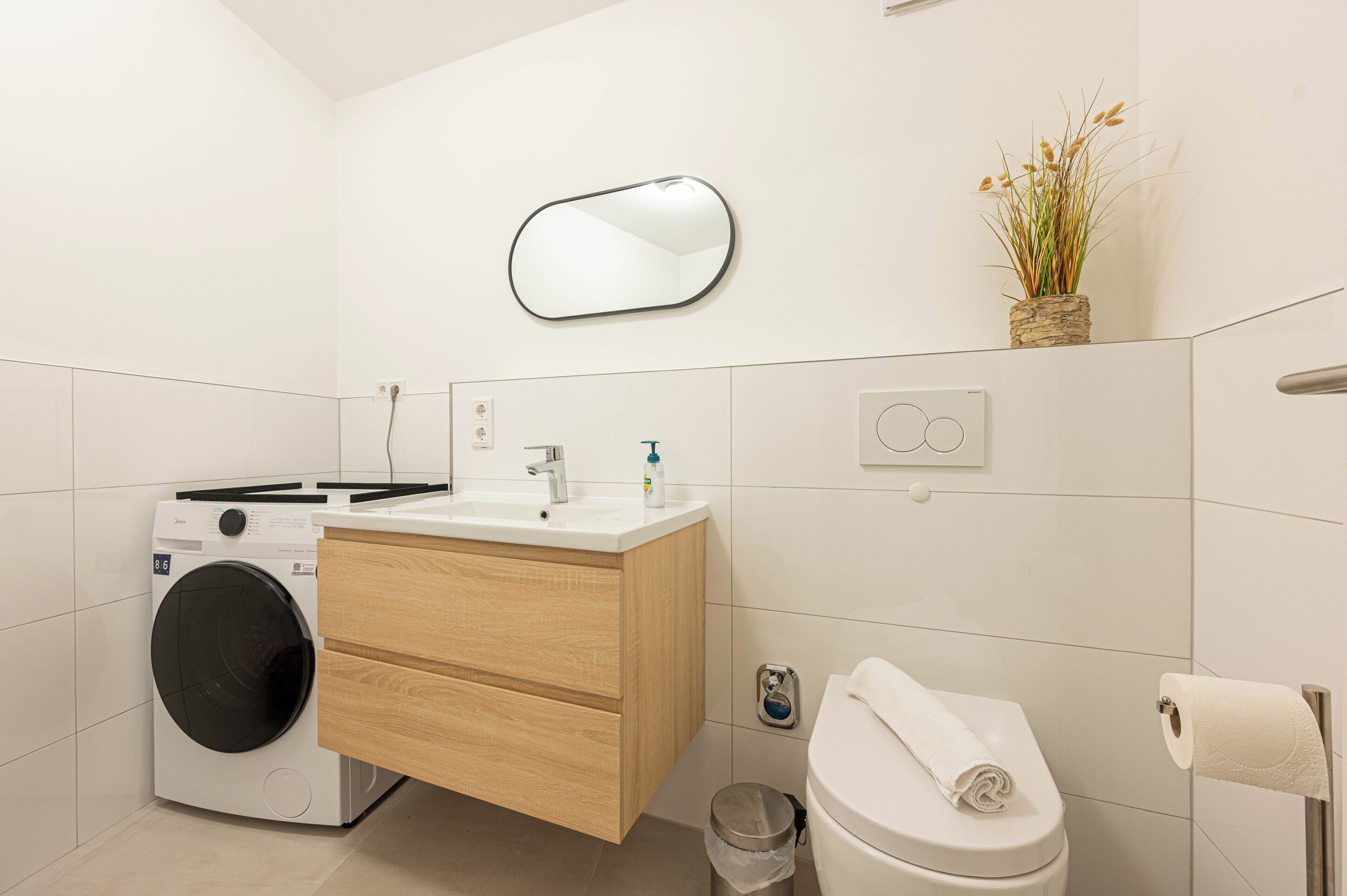 Ein modernes Badezimmer mit Waschmaschine, Holzwaschbecken, Toilette und Spiegel.