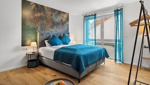 A bedroom with a bed, a large abstract painting, a window with curtains, and a wooden floor. - Lit Living-Luxury-Box Spring - Parking (Hemsbach)