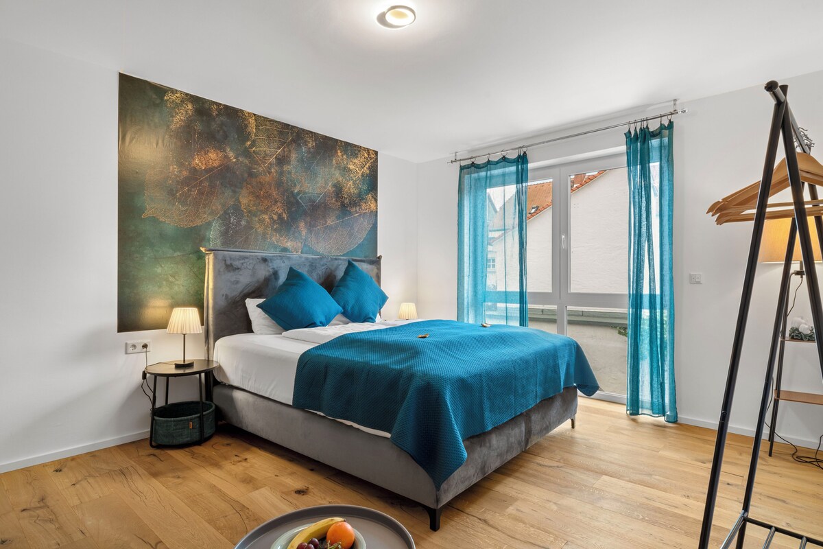Ein Schlafzimmer mit einem Bett, einem großen abstrakten Gemälde, einem Fenster mit Vorhängen und Holzboden.