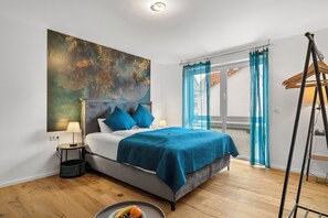 Une chambre à coucher avec un lit, un grand tableau abstrait, une fenêtre avec des rideaux et un plancher en bois.