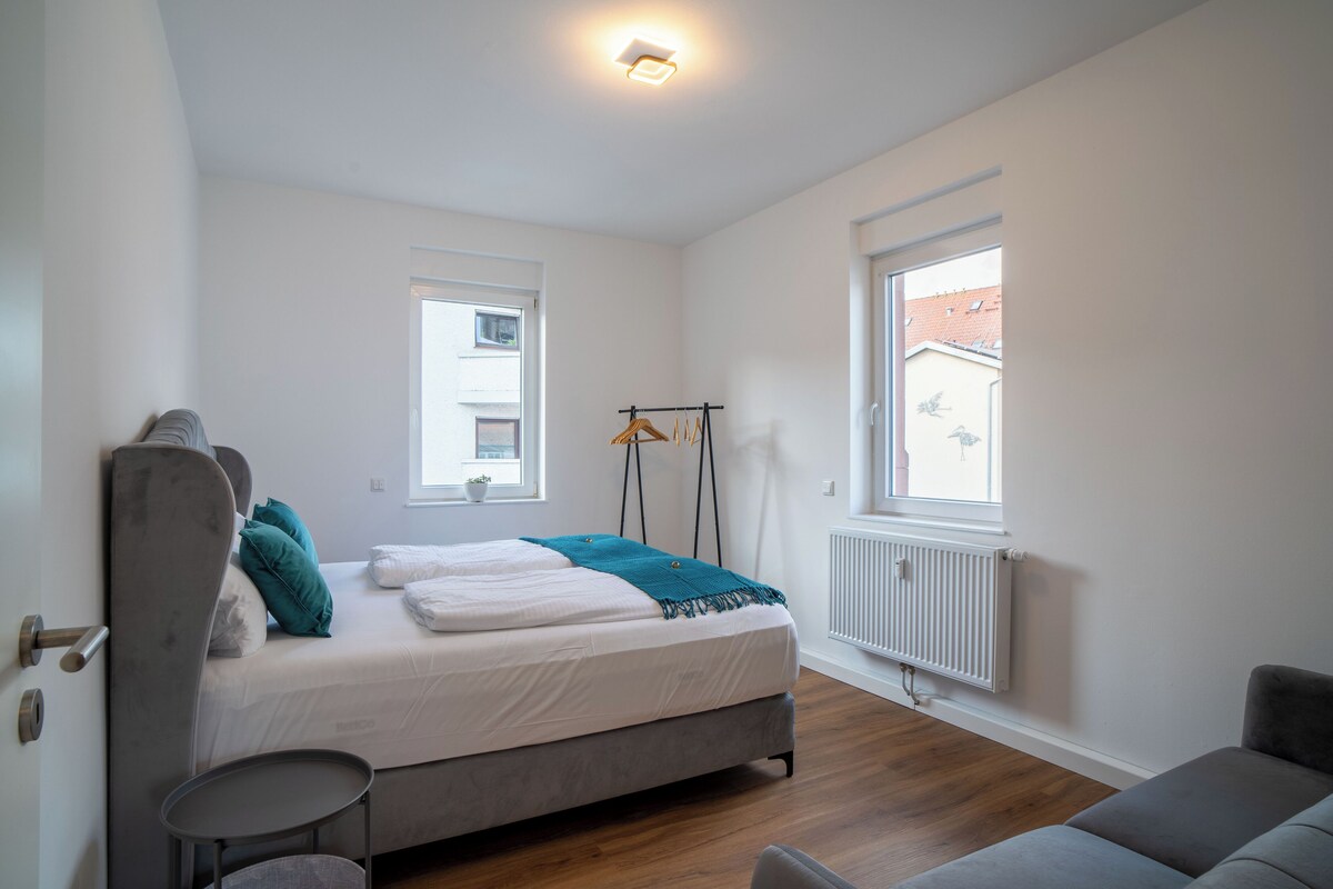 Ein Schlafzimmer mit Bett, Sessel, Heizkörper und Fenster.
