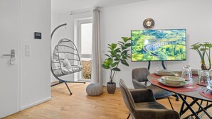 A modern living room with a dining area, a hanging chair, potted plants, and a large TV on the wall. - Lit Living-Luxury-Box Spring - Parking (Hemsbach)