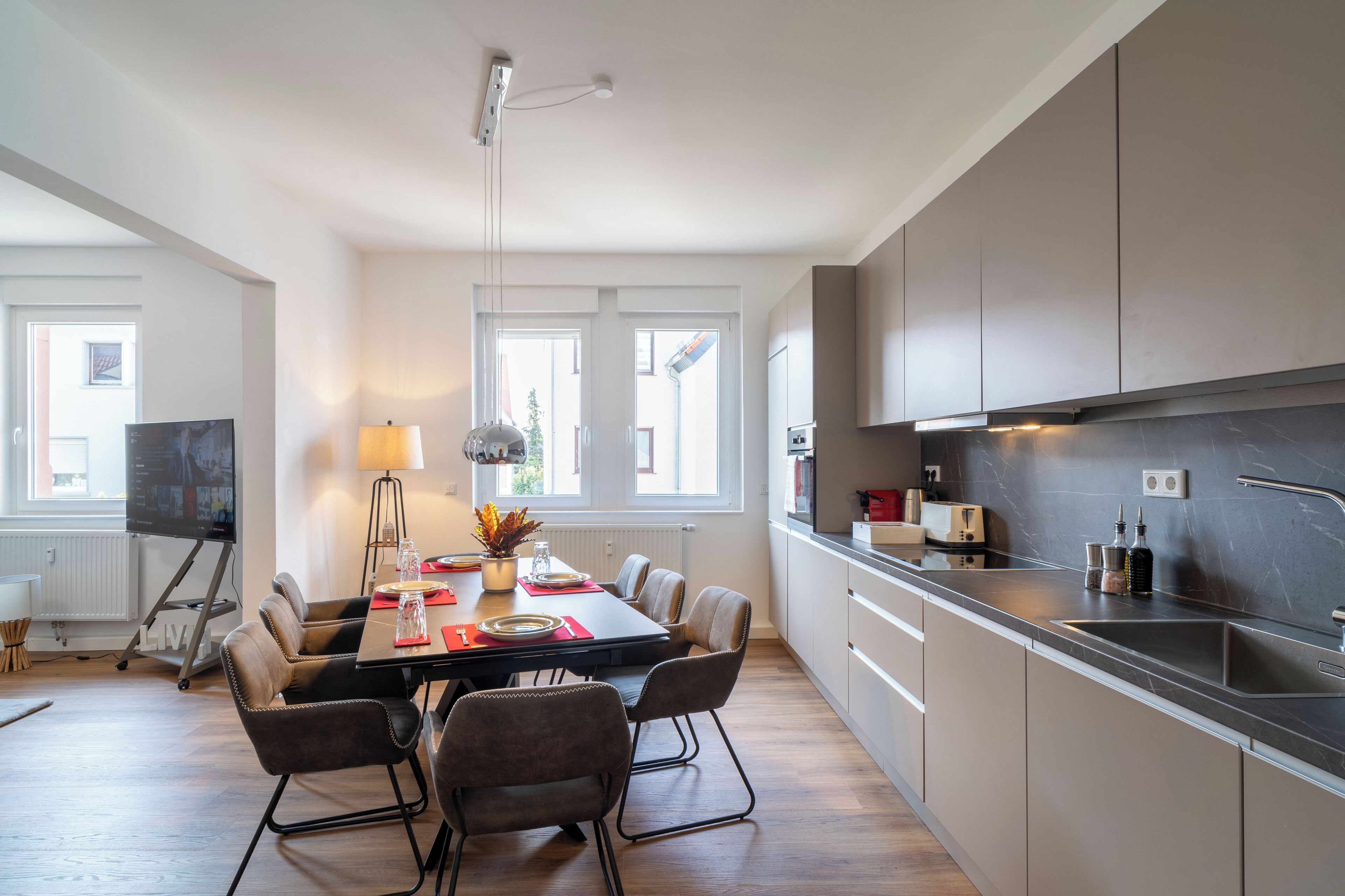 Une cuisine moderne avec un coin repas, de grandes fenêtres et un téléviseur à écran plat.