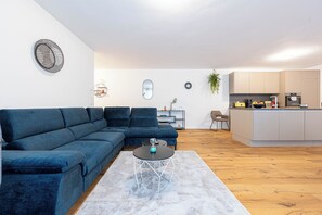 Una sala de estar moderna con un sofá modular, una mesa de centro y una cocina con mostrador y armarios.