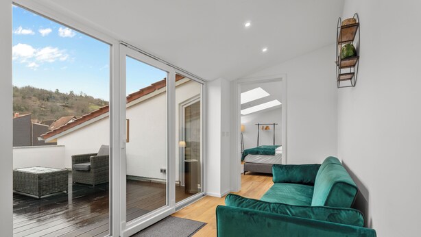 A modern living room with a green sofa, a dining area with a table and chairs, and a sliding glass door leading to an outdoor deck. - Lit Living-Luxury-Box Spring - Parking (Hemsbach)