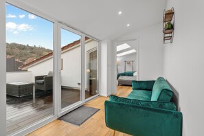 Een moderne woonkamer met een groene bank, een eethoek met een tafel en stoelen, en een schuifdeur die leidt naar een terras.