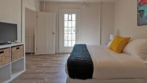 A bedroom with a bed, a television on a stand, and a door leading to another room. - Colorful Modern Hideaway In Downtown Woodstock - AC & WiFi (Woodstock)