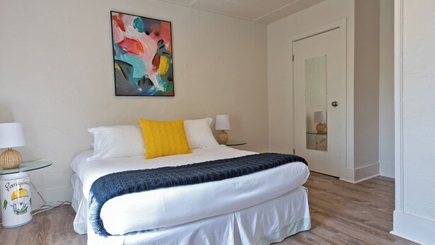 Un dormitorio ordenado con cama, lámpara de noche y un colorido cuadro abstracto en la pared.