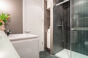 A modern bathroom with a glass-enclosed shower, a white sink, and a vase with flowers. - Be London - The Covent Garden Residences (London)