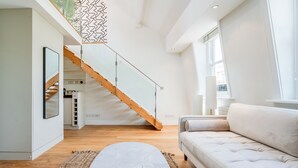 Una sala de estar moderna con una escalera de madera, un sofá blanco y una mesa de centro de mármol.