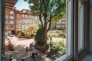 Ein Innenhof mit Bänken, einem großen Baum und Blick auf rote Backsteingebäude.