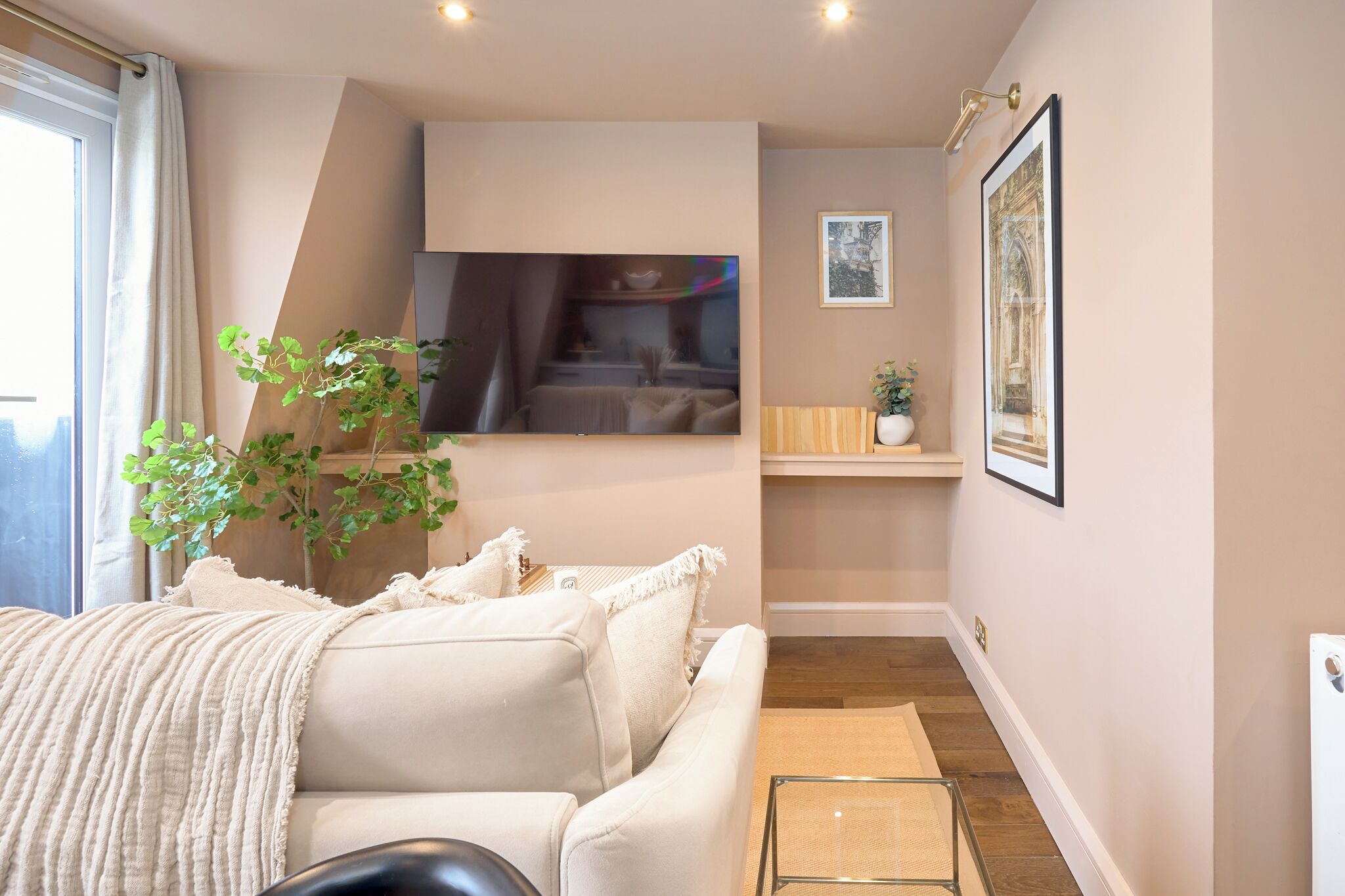 A modern bedroom with a sofa, a small table, a plant, and a framed picture on the wall.