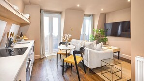 A modern apartment with a kitchen, dining area, and living room. It features a large window, a flat-screen TV, and a cozy seating arrangement. - Be London - St John's Wood Residences (London)