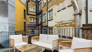 An outdoor seating area with wicker furniture and a glass-top table, surrounded by a wooden deck and metal railings. - Be London - Piccadilly Circus Residences (London)