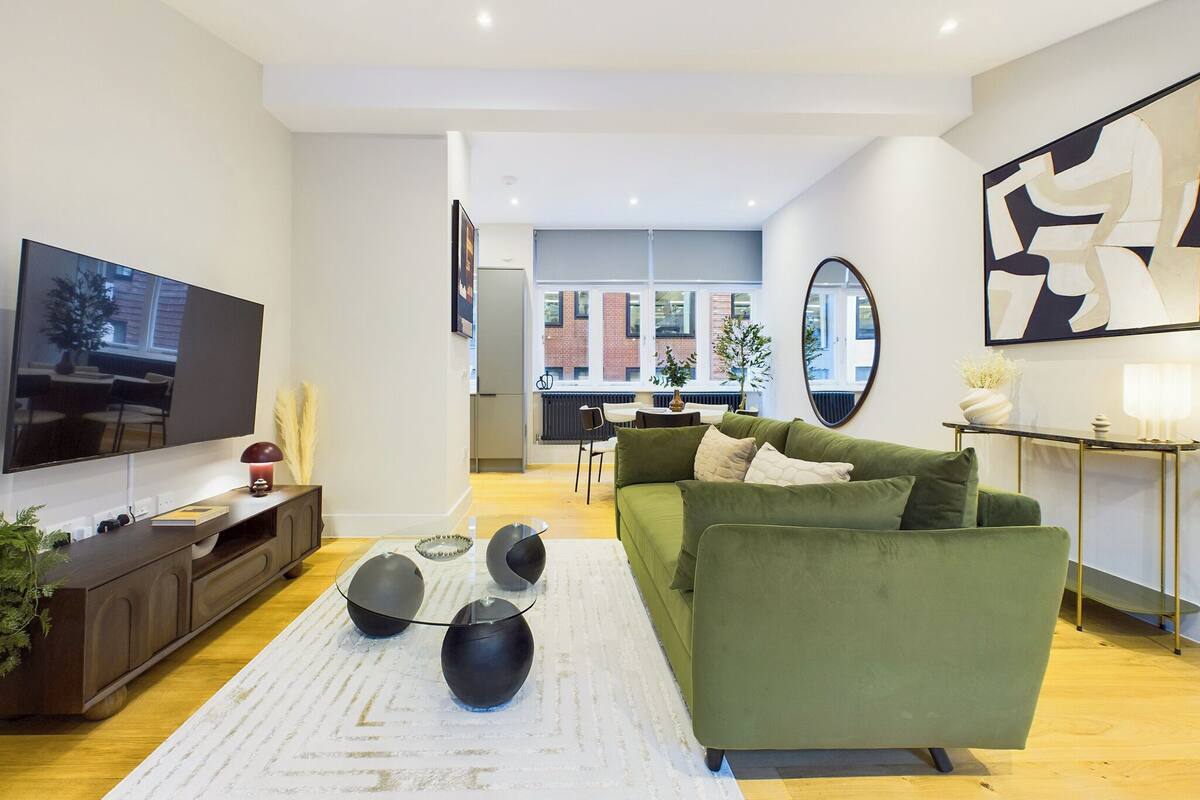 A modern living room with a flat-screen TV, a green sofa, and a coffee table with spherical black objects.