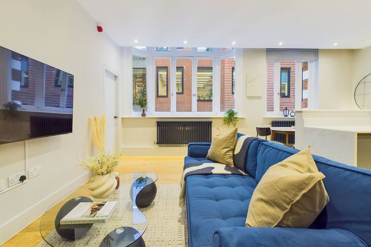 A modern living room with a blue sofa, a glass coffee table, and a flat-screen TV mounted on the wall.