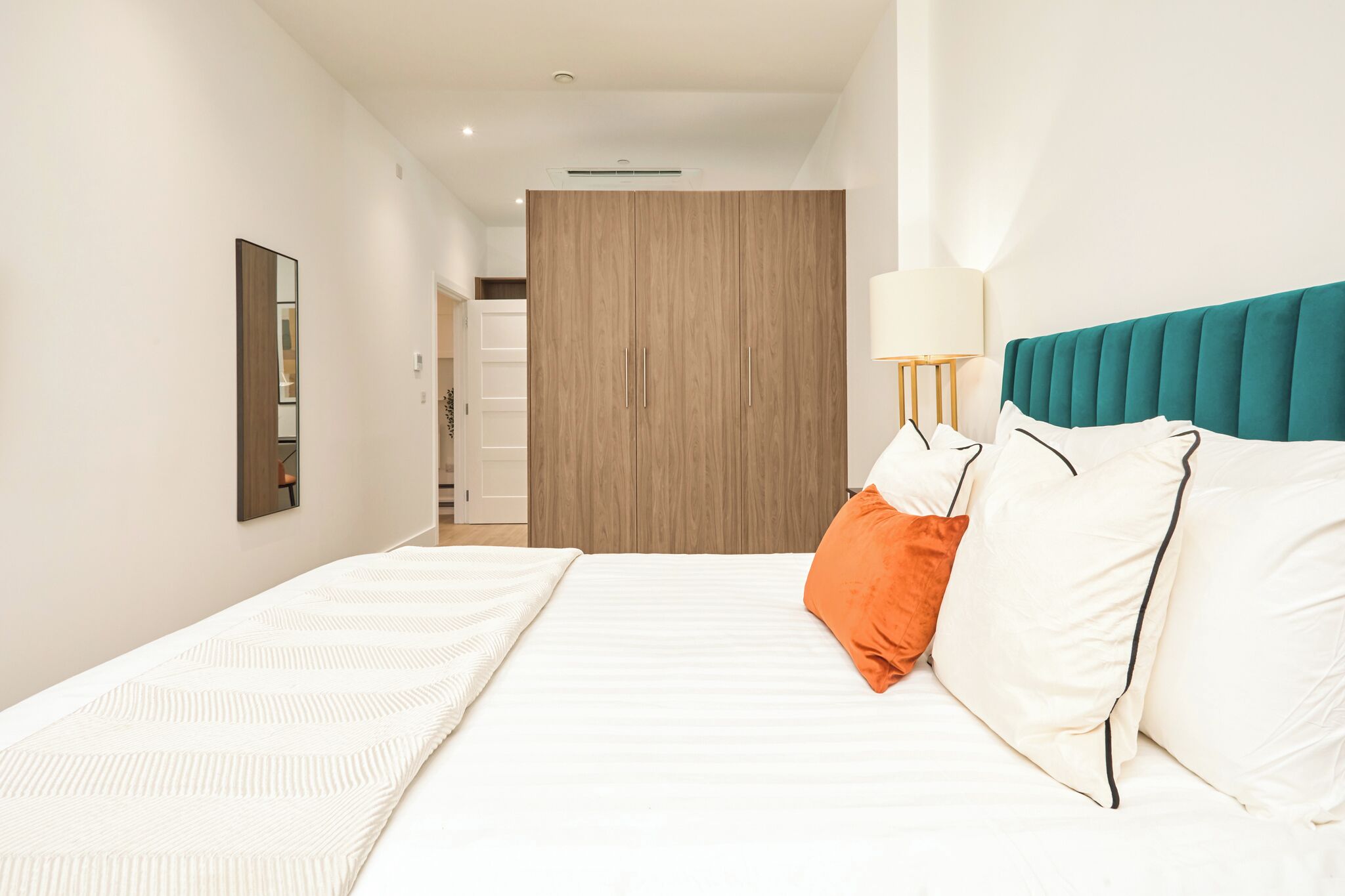Une chambre d’hôtel moderne avec un grand lit, une armoire en bois, une table de chevet avec une lampe et un miroir au mur.