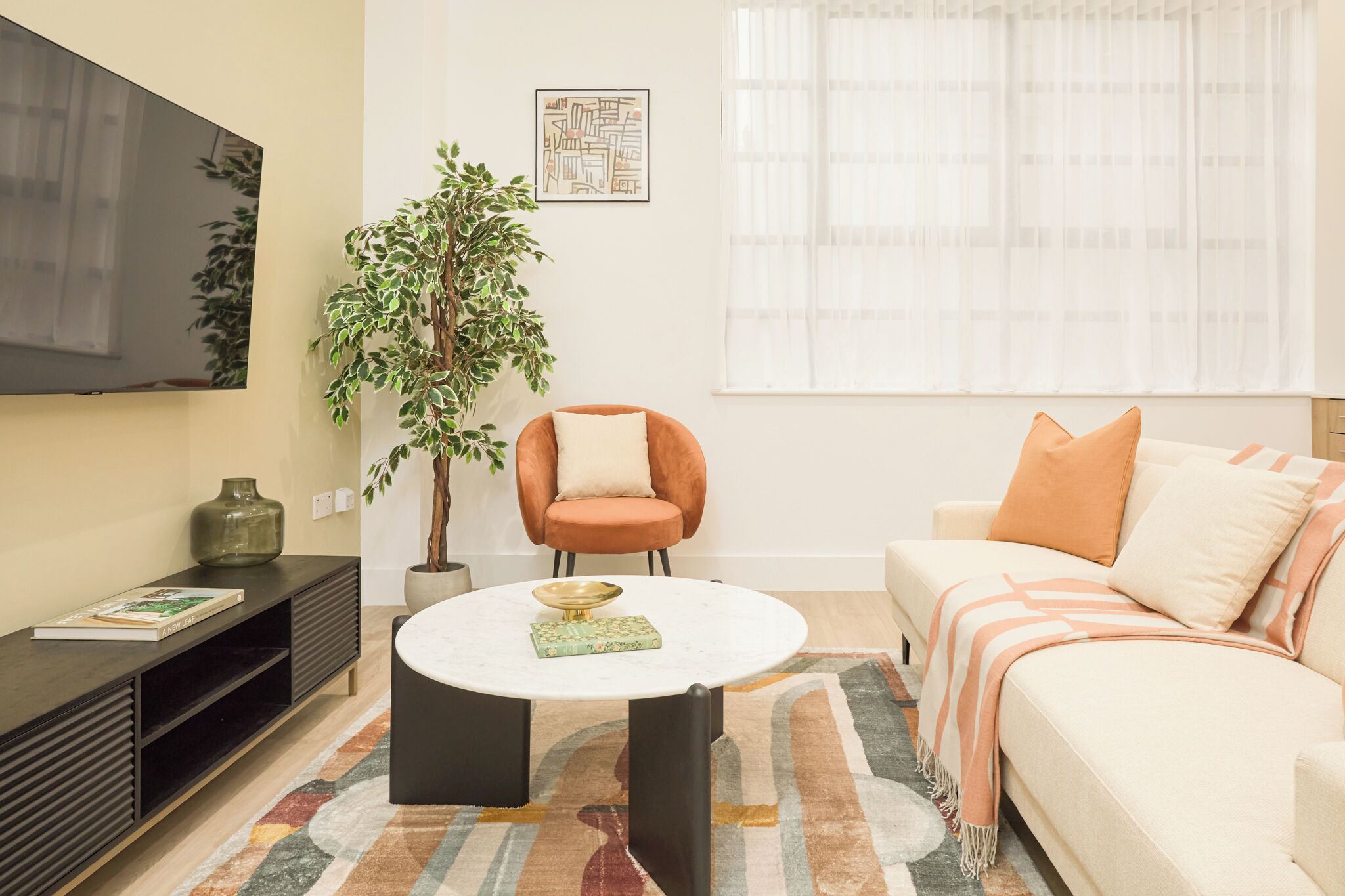 A living room with a sofa, armchair, coffee table, TV, and a potted plant.