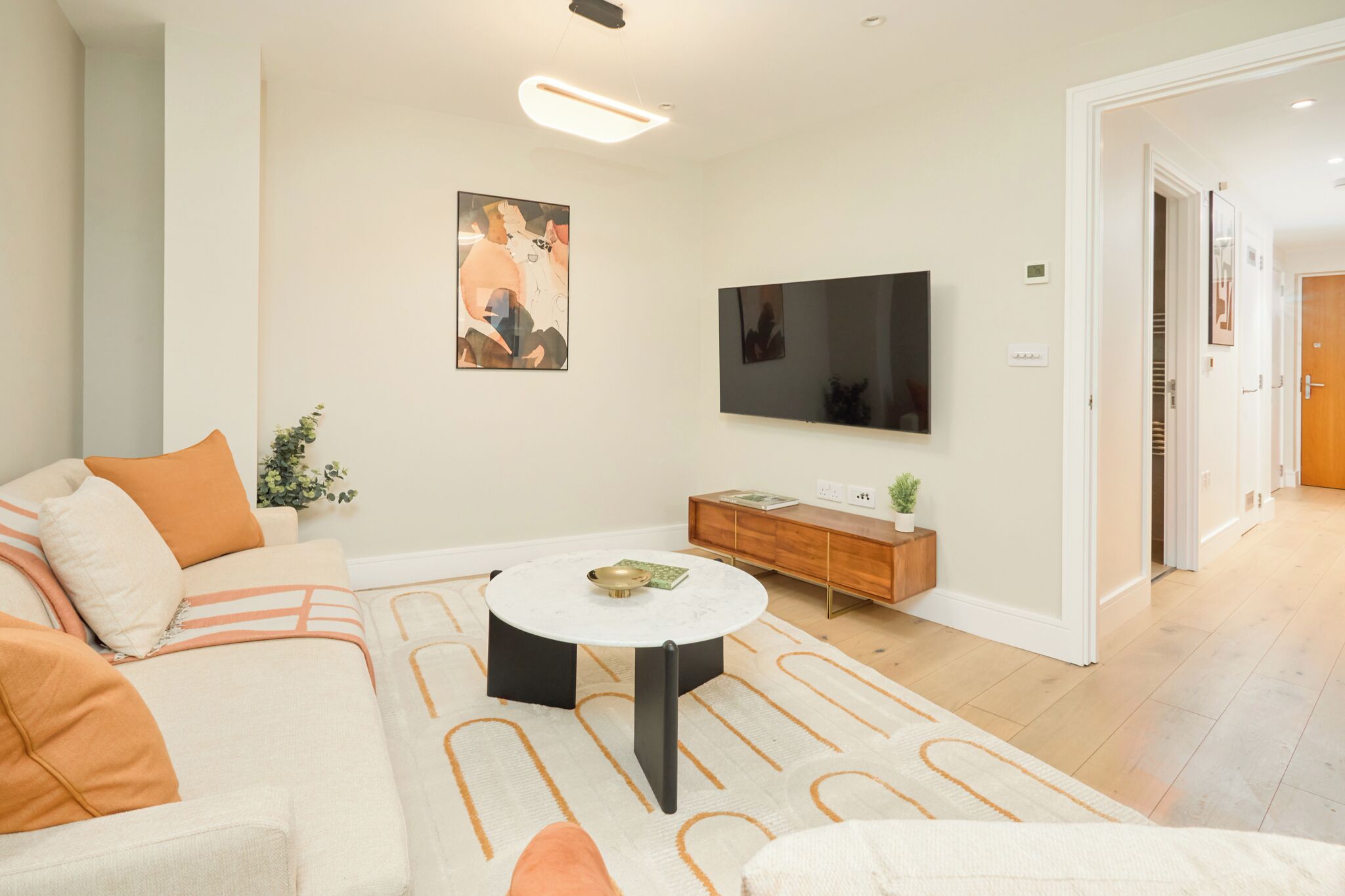 A modern living room with a sofa, coffee table, TV, and a hallway leading to a door.