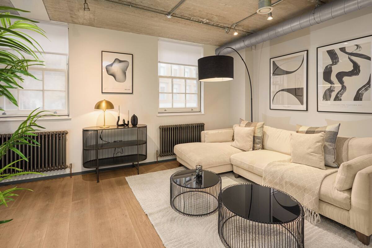 Un salon moderne avec un canapé d’angle beige, des tables basses en métal noir et des œuvres d’art abstraites accrochées au mur.