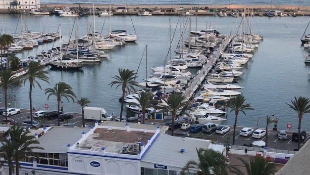 A marina with numerous boats docked, a building with a blue and white facade, and palm trees in the foreground. - Estepona Marina Apartment, Costa Del Sol (Estepona)