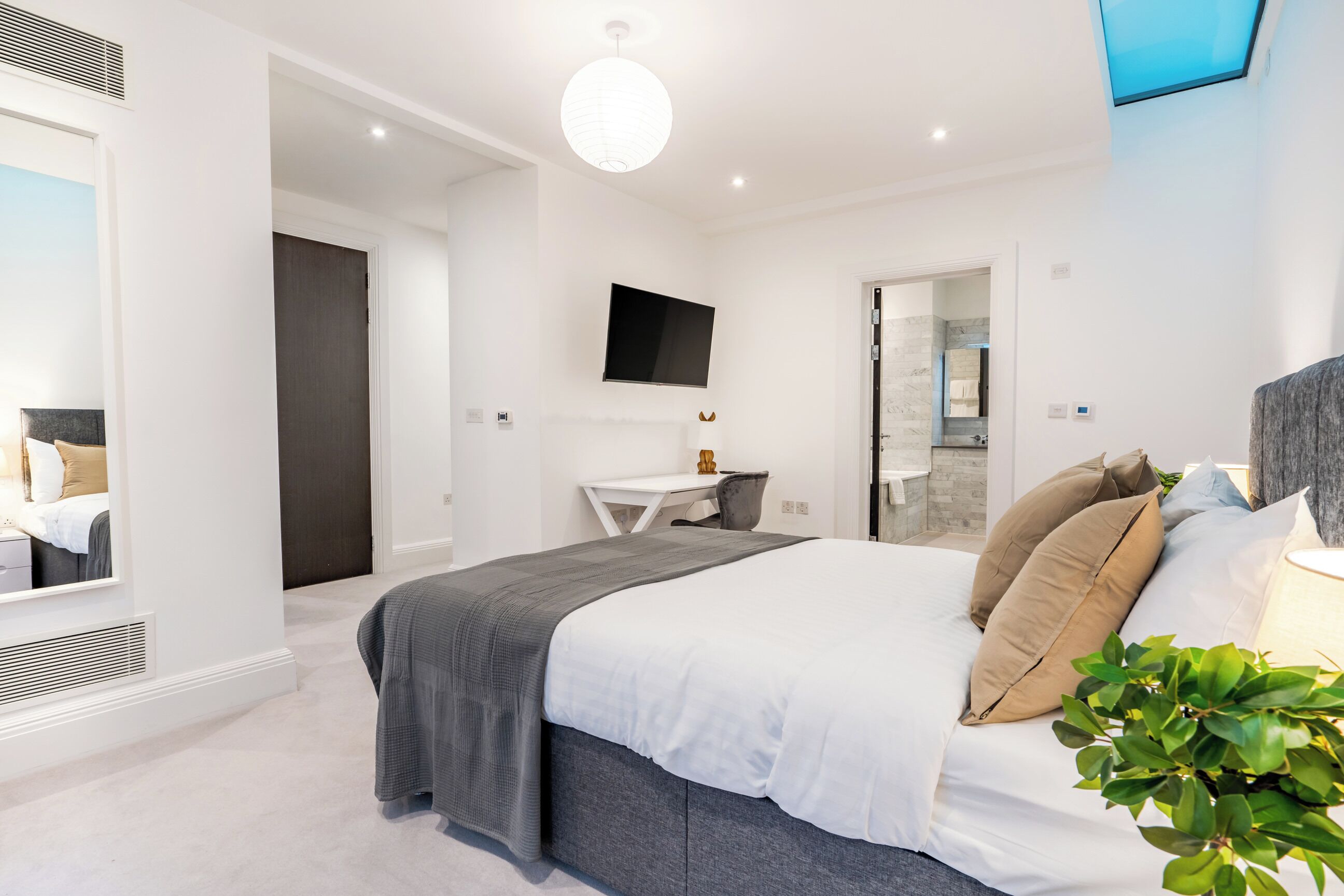 A modern bedroom with a bed, a desk, and a TV.