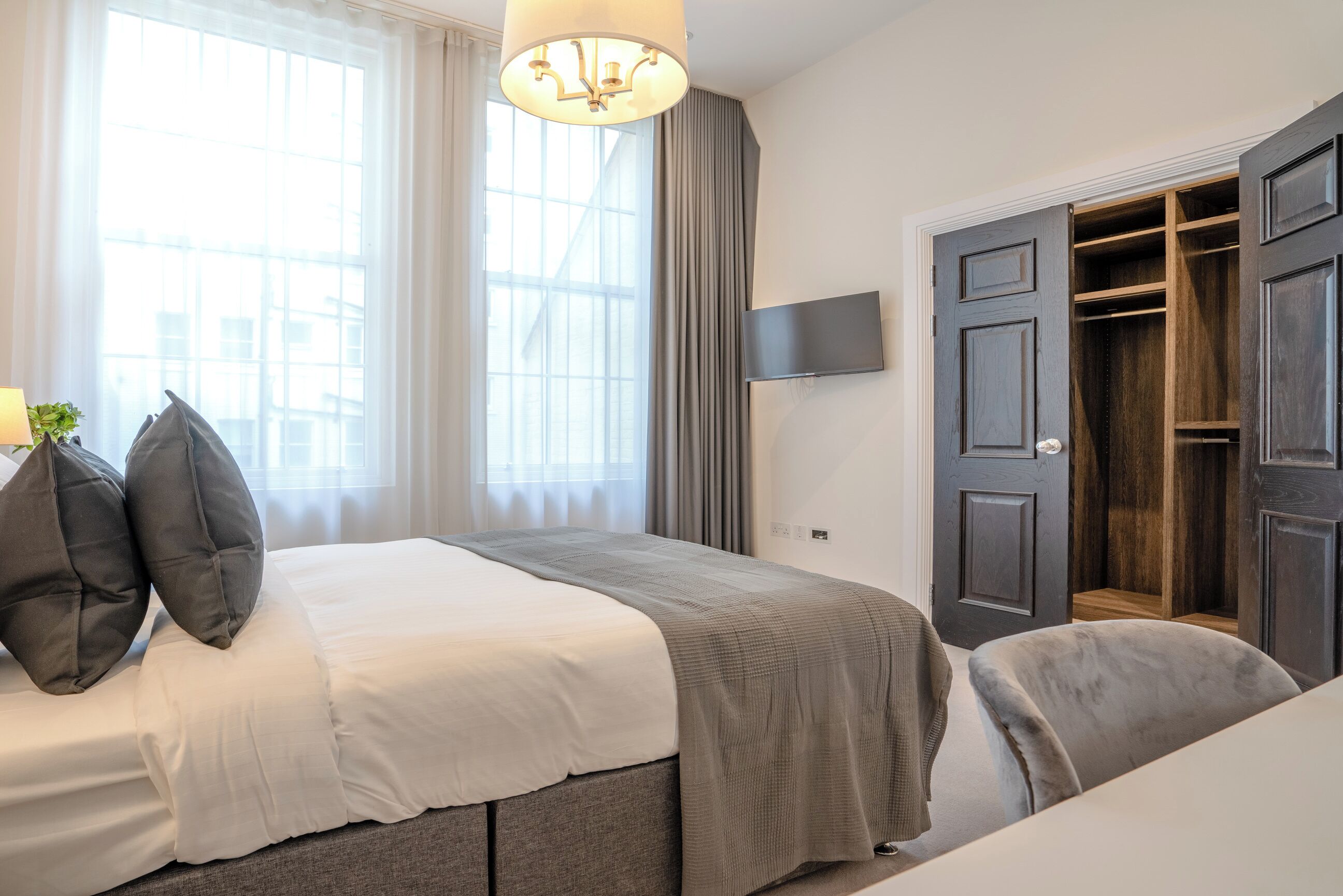 A bedroom with a bed, a TV, a wardrobe, and a window with curtains.