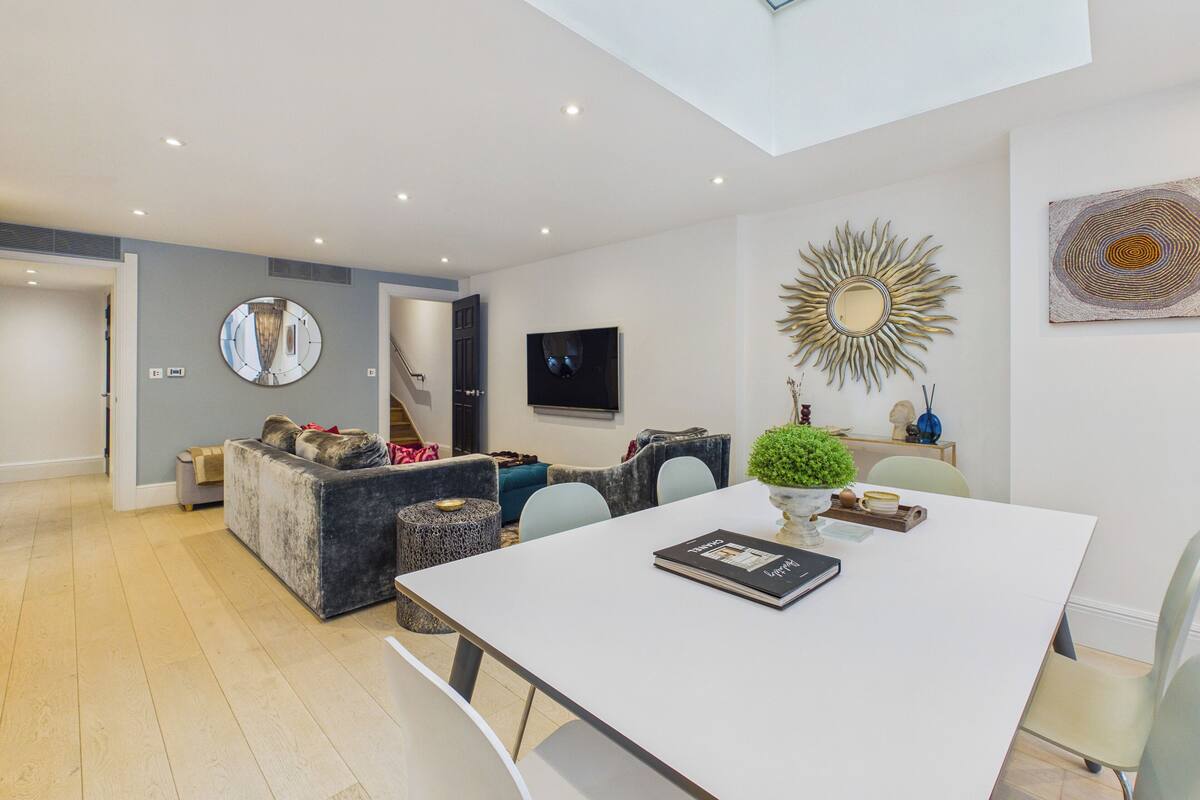 A modern living room with a dining area, a large mirror, and a television on the wall.