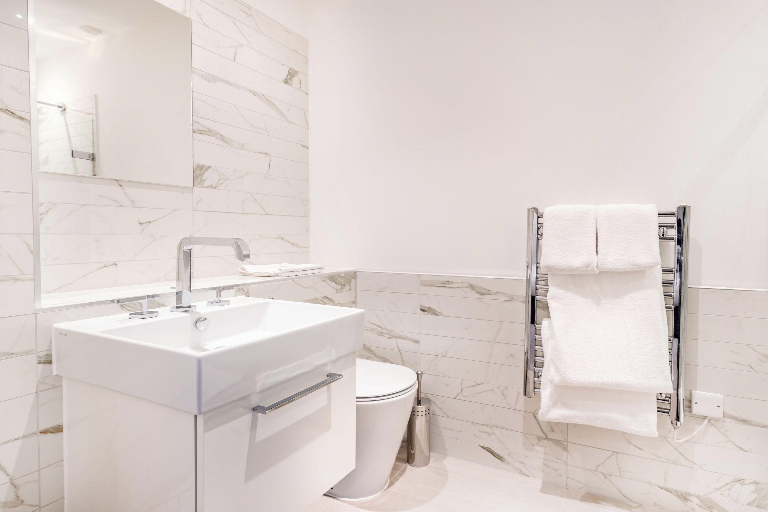 A modern bathroom with a white sink, toilet, and towel rack.