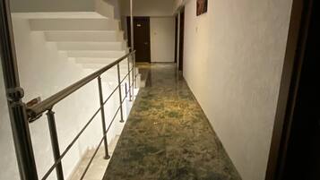 A hallway with a marble floor, a staircase with a metal railing, and a door at the end.