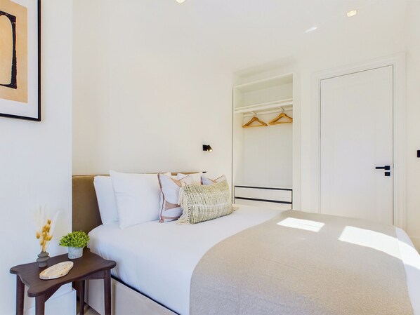 A modern bedroom with a bed, bedside table, and a walk-in closet. - Be London - The Maida Vale Residences (London)