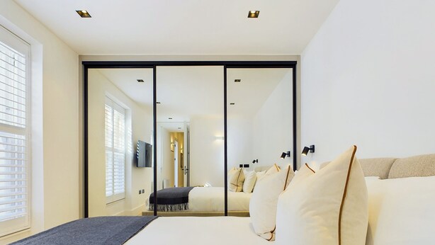 Een moderne hotelkamer met een groot bed, een schuifdeurkast en uitzicht op de gang.