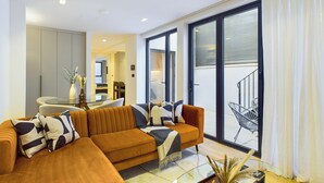 Een moderne woonkamer met een grote bank, een glazen salontafel en uitzicht op een balkon met een stoel.