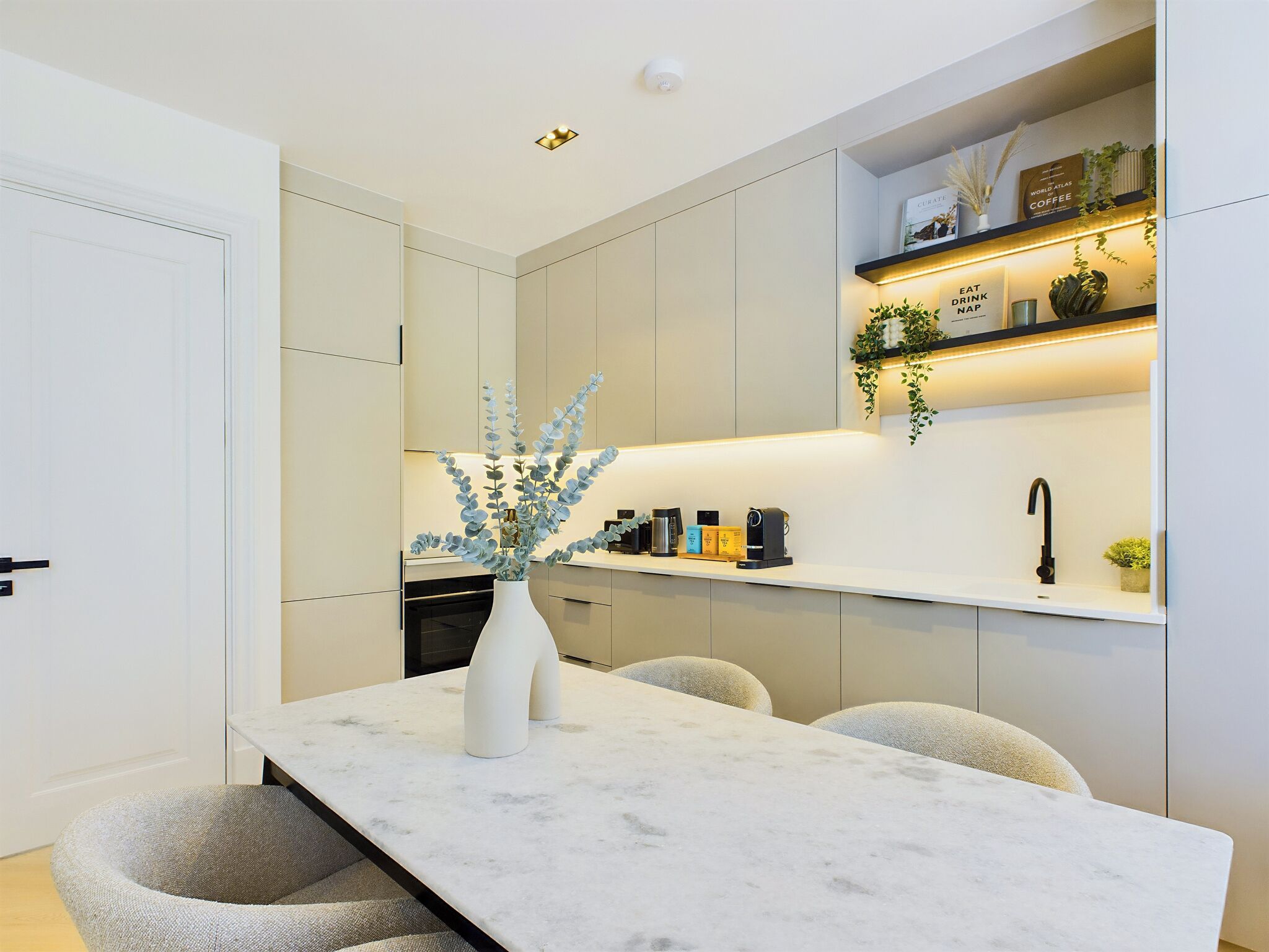 A modern kitchen with a marble countertop, a vase with a plant, and a coffee machine.
