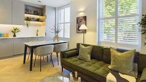 Een moderne keuken met witte kasten, een eethoek met een tafel en stoelen, en een groene bank met kussens.